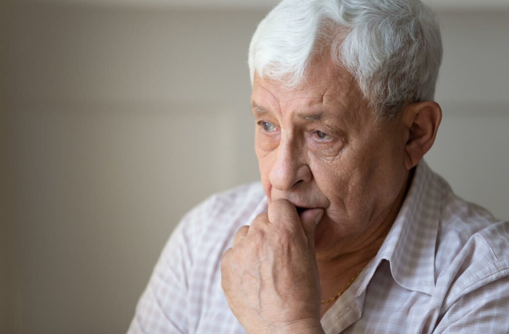An elderly man deeply brooding with his mouth resting on his hand trying to remember something.