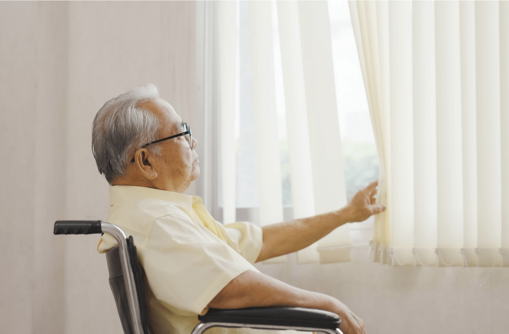 A senior citizen man in a wheelchair, looking out a window