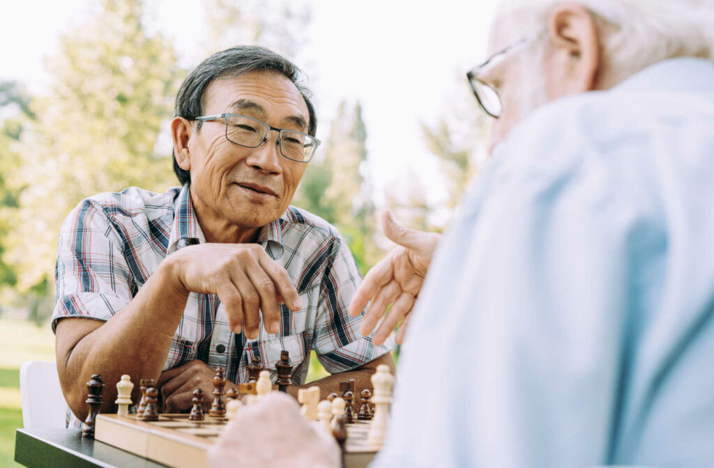 Two senior men sitting across from each other at a table playing a game of chess in a park.