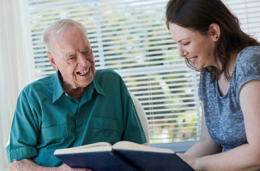 A senior man and his daughter smiling while looking at a photo album together.