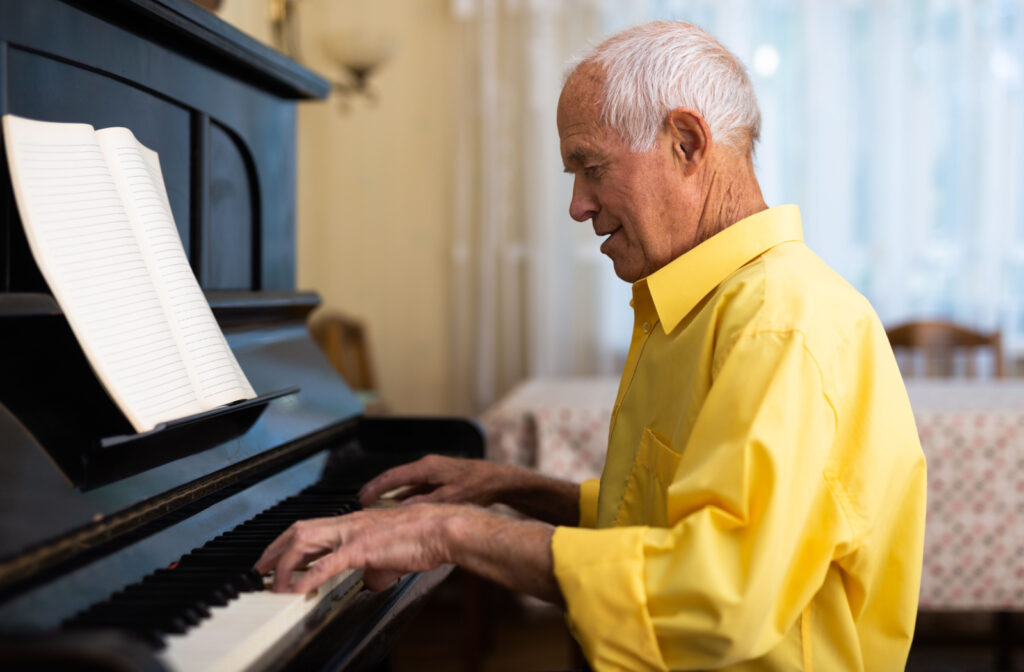 An older adult man wearing yellow polo shirt and playing a piano at home