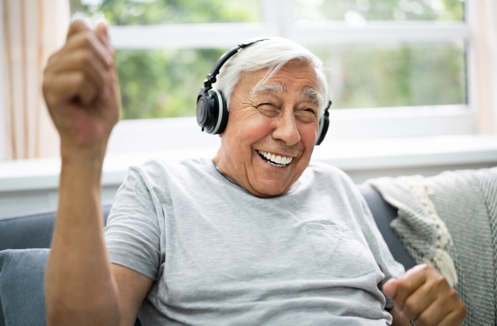 An older adult man sitting on a couch wearing headphones and listening to music.