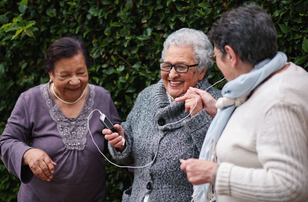 A group of older adult women smiling and listening to music on a smartphone while wearing earphones