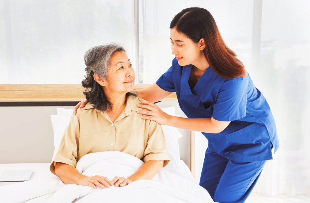 a caregiver helping an elderly woman to sit up on her bed.