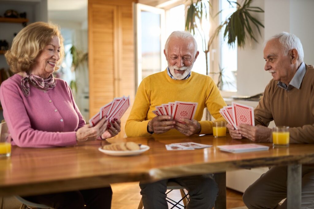 Three older adults sit together, enjoying a card game to train their memory.