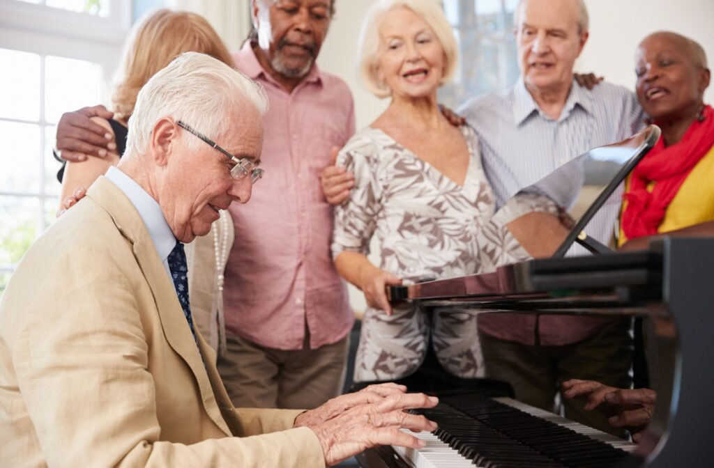 A group of older adults gathers to sing around a piano, with one senior playing chords.